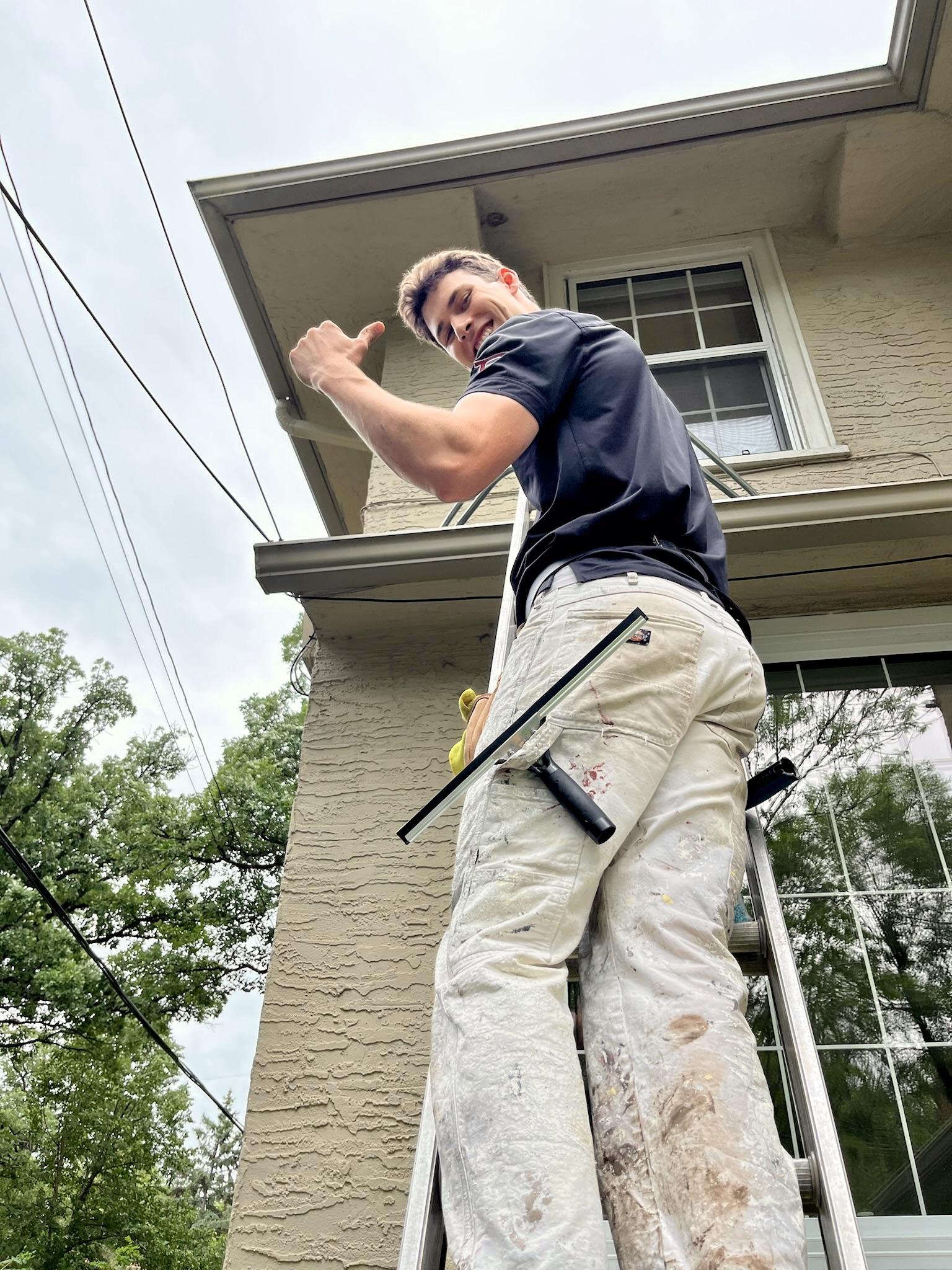 Bubble Brothers team member smiling on a ladder with a window-cleaning squeegee
