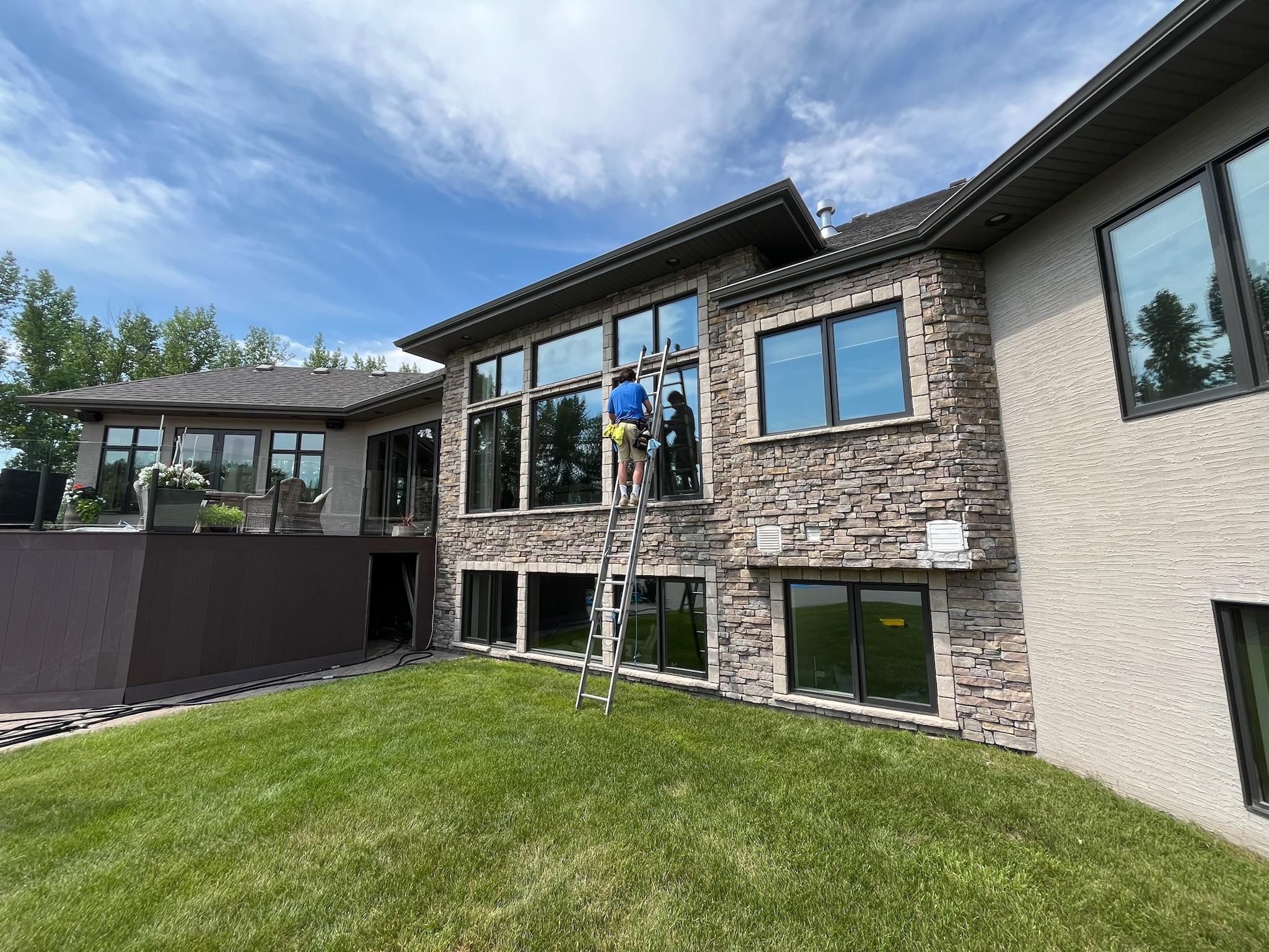 Bubble Brothers team member cleaning large windows from a ladder on a stone-clad home
