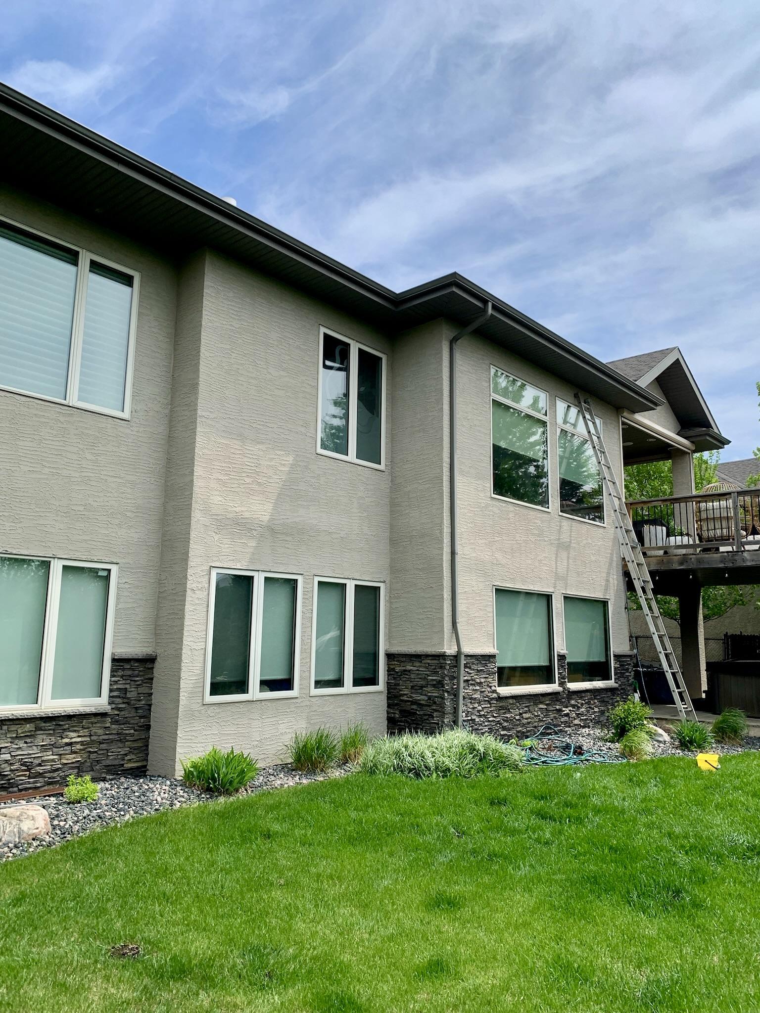Large windows on a two-storey home with a ladder set up beside the deck