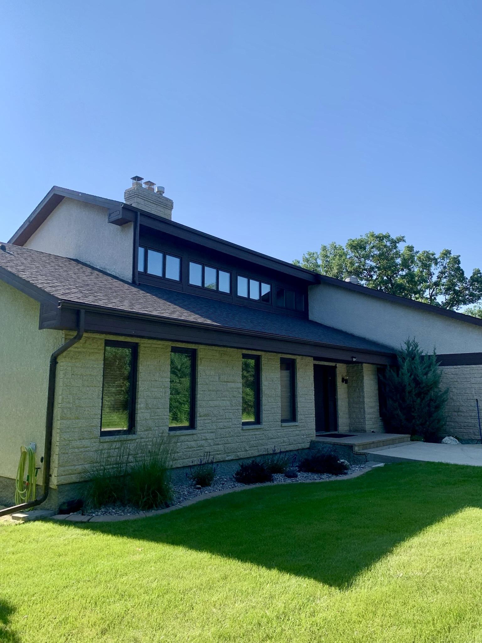 Tall exterior windows and upper clerestory windows on a stone-front home beside a green lawn