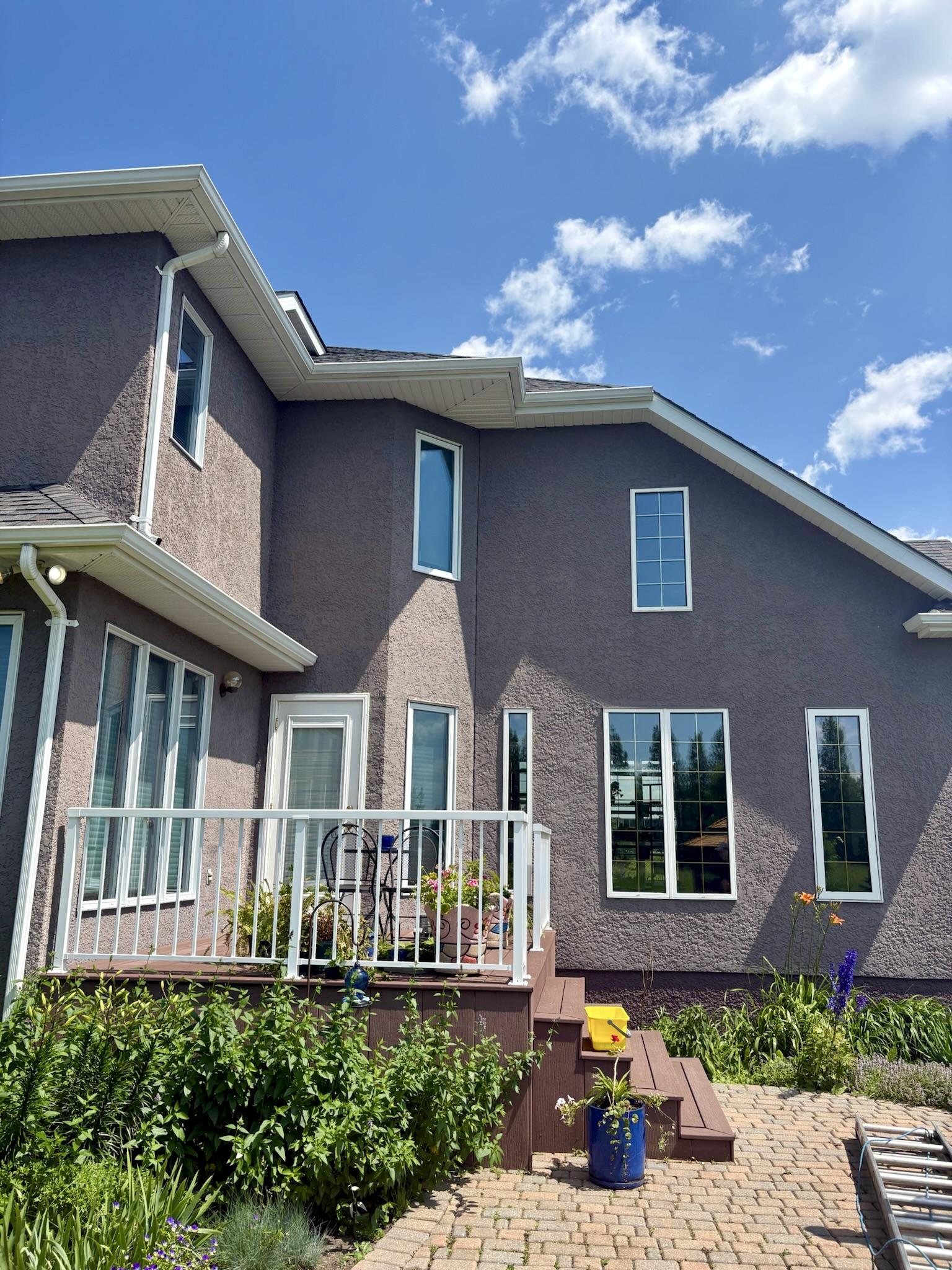 Tall windows reflecting blue skies on a stucco home beside a garden and deck