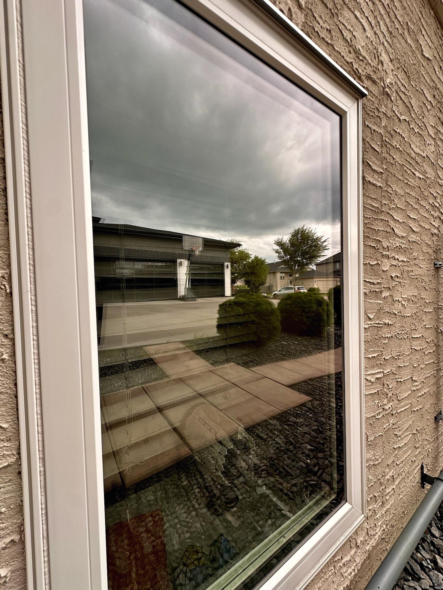 Close-up of a white-framed window reflecting nearby homes and landscaping