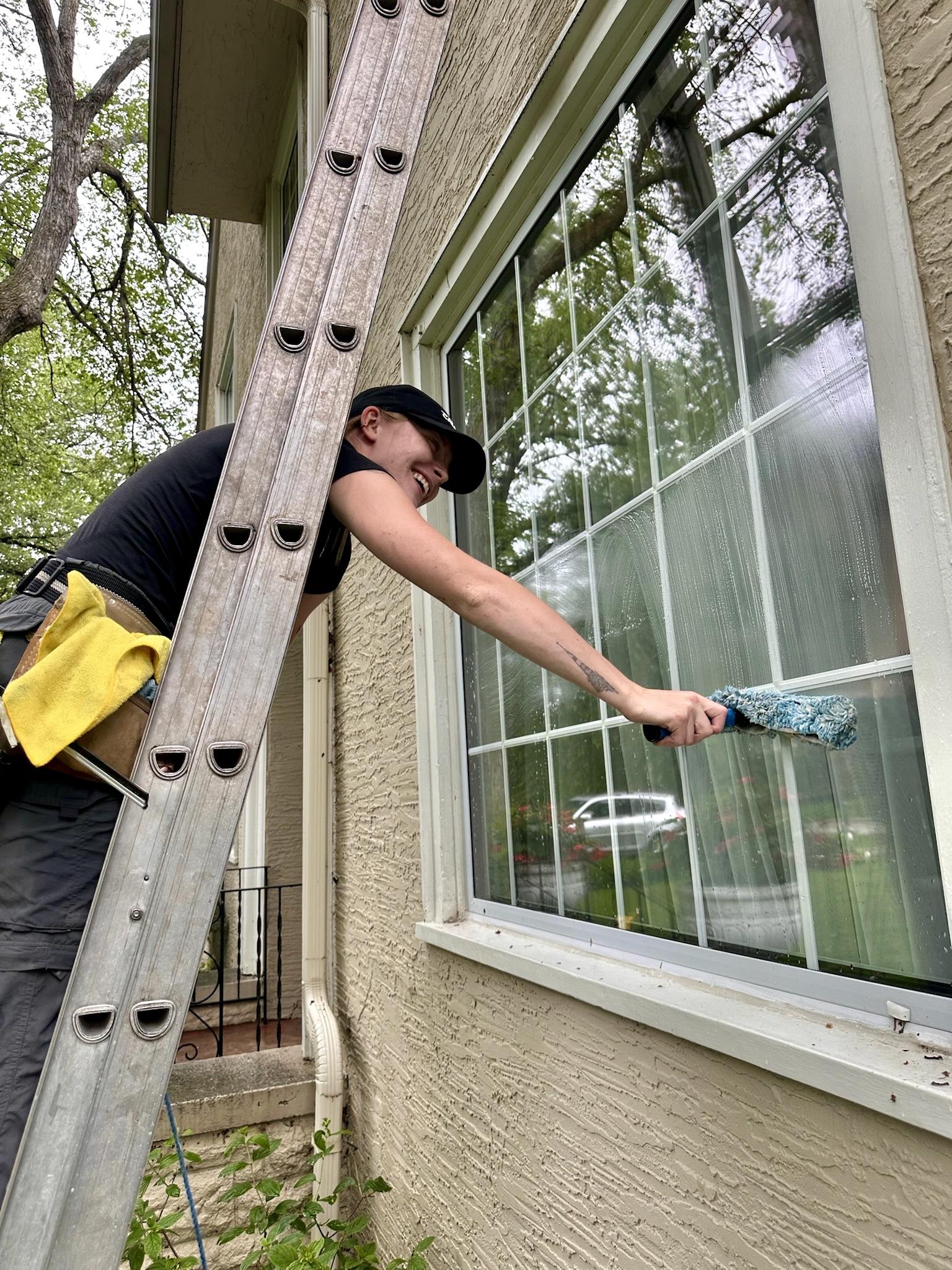 Bubble Brothers team member scrubbing a residential window with a washer beside a ladder