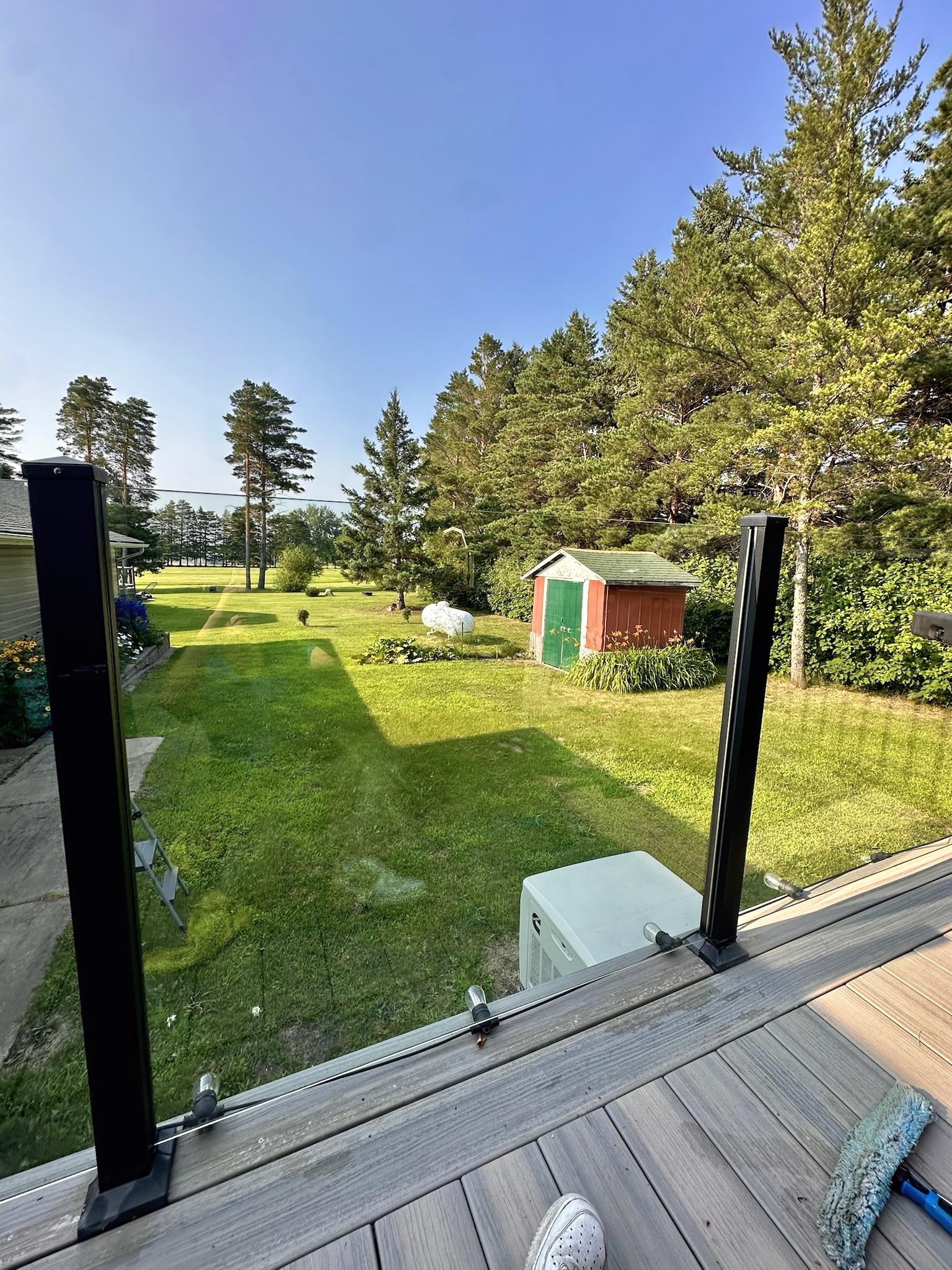 Glass deck railing overlooking a green lawn, trees, and a lake